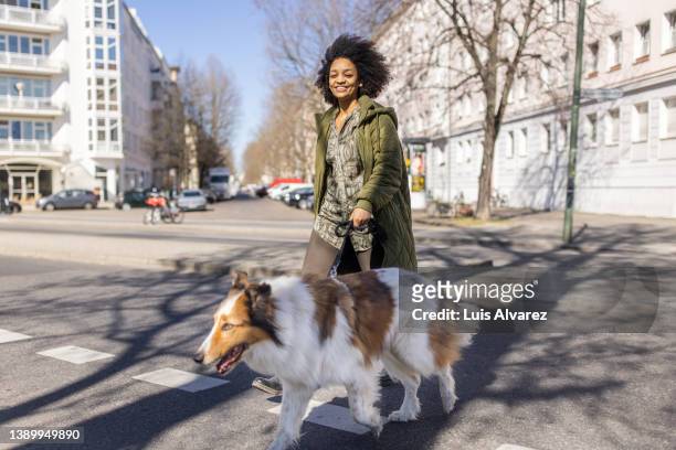 smiling young african woman walking her dog in the city - green coat stock pictures, royalty-free photos & images