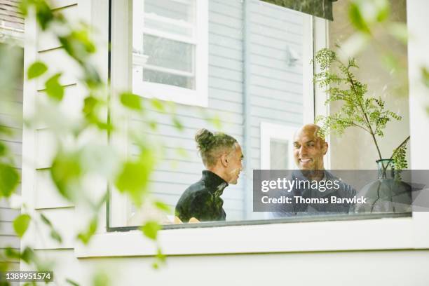 medium wide shot view though window of smiling father and son in discussion while sitting in living room - adult helping teenager stock pictures, royalty-free photos & images