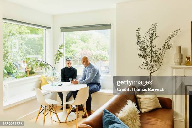 wide shot of father and son looking at information on smart phone while sitting in living room - black polo shirt stock pictures, royalty-free photos & images