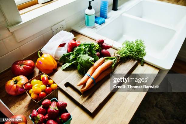 medium shot high angle view of fresh organic vegetables and fruit on counter next to sink in kitchen - cutting board stock pictures, royalty-free photos & images