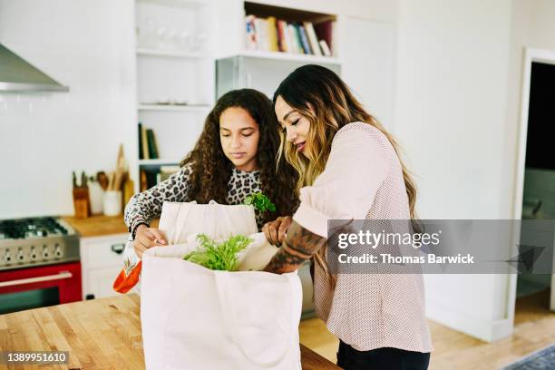 medium shot of mother and daughter unloading groceries in kitchen after shopping - herbruikbare tas stockfoto's en -beelden