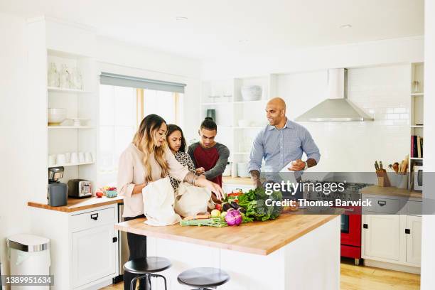 wide shot of family unloading fresh produce in kitchen after shopping - indian arrival stock pictures, royalty-free photos & images