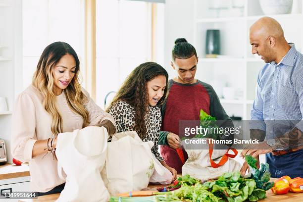 medium shot of family unloading fresh produce in kitchen after grocery shopping - body art stock pictures, royalty-free photos & images
