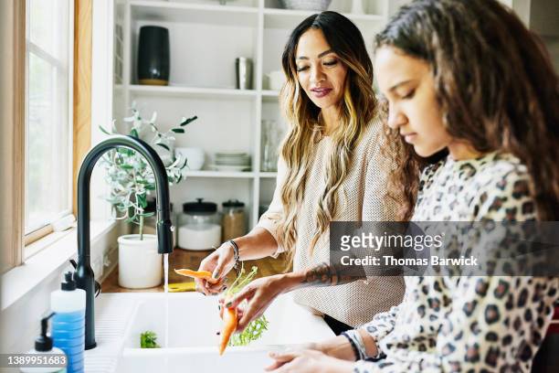 medium shot of mother washing fresh vegetable in kitchen sink with daughter - friends clean stock pictures, royalty-free photos & images