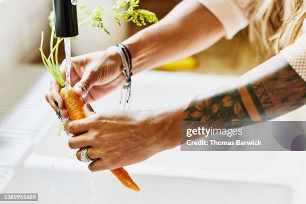 medium close up shot of womans hands washing organic carrot in kitchen sink - indian food bildbanksfoton och bilder