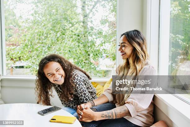 medium shot of mother and daughter laughing together while hanging out in living room - blusa bege - fotografias e filmes do acervo