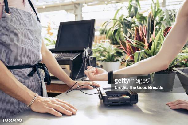 woman making mobile payment with smart watch at garden center - smartwatch pay stock-fotos und bilder
