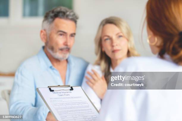 doctor filling out medical insurance form with mature couple - claim form stock pictures, royalty-free photos & images
