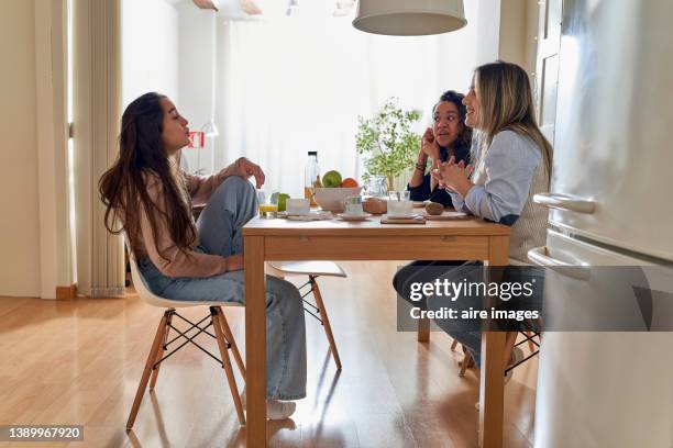 female friends sitting at dining table, having breakfast in apartment with minimalist decor, in the background sunlight coming through the curtains. - parceiro de apartamento - fotografias e filmes do acervo