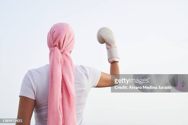 unrecognizable female cancer patient with pink headscarf and boxing gloves in her hands as a sign of fight and strength. concept of fighting and beating cancer. - roze handschoen stockfoto's en -beelden