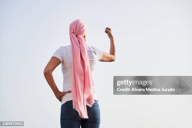 unrecognizable female cancer patient with a pink scarf on her head, on her back with her arms raised as a sign of strength and victory. concept of fighting and beating cancer. - best bosom fotografías e imágenes de stock