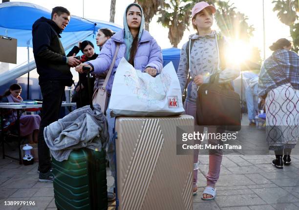 Ukrainians who are seeking asylum in the United States stand with their belongings at a makeshift encampment near the U.S.-Mexico border as the sun...