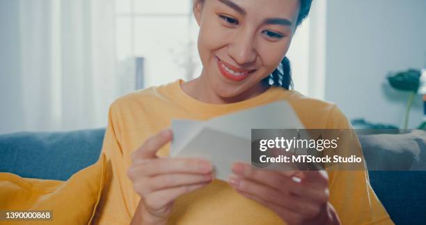 young asian woman feel excited unpacking gift box sitting on couch in living room at home. - birthday greeting card stock pictures, royalty-free photos & images