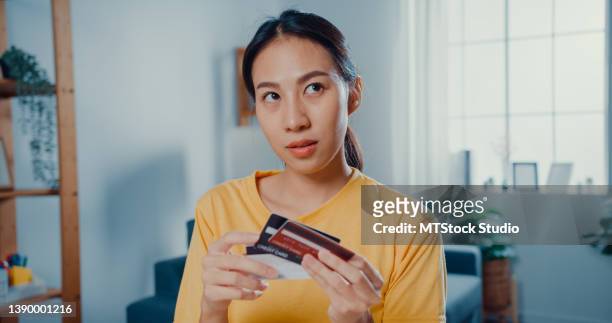 young asian woman holding credit card making payment online sitting at desk in living room at home. - debit card fraud stock pictures, royalty-free photos & images