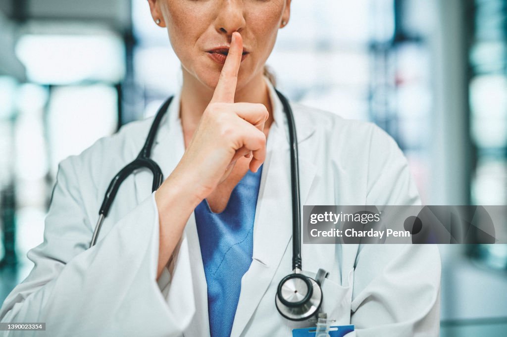 Shot of a doctor with her finger on her lips in a modern hospital