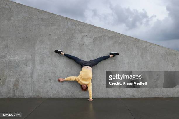 ballet dancer practicing cartwheel against gray wall - spagat stock-fotos und bilder