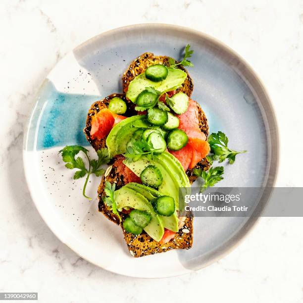 wholegrain crackers with smoked salmon, avocado, and cucumbers on a plate on white background - coriandre fond blanc photos et images de collection