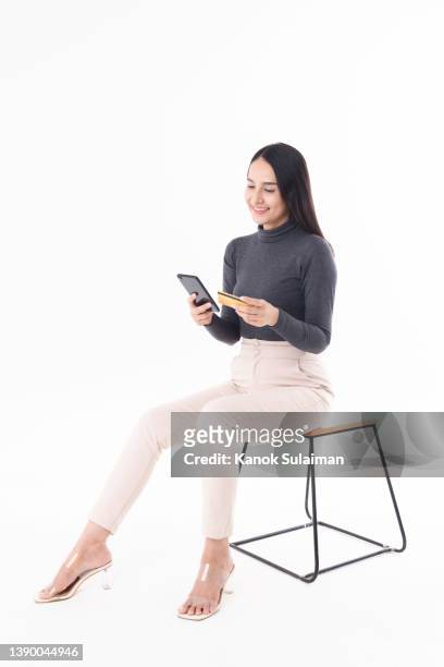 young woman with credit card online shopping while using smart phone against white background - sitting and using smartphone studio stock-fotos und bilder
