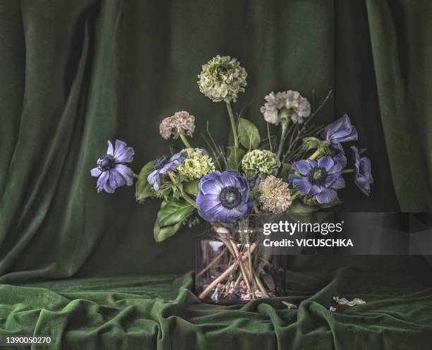 beautiful flower bouquet with purple anemone fower and snowball flower in glass vase at dark green fabric background - anemone flower arrangements stock pictures, royalty-free photos & images