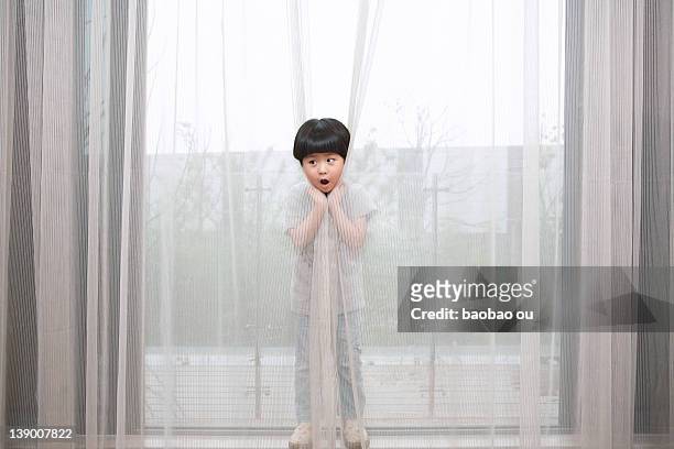 little boy hiding behind curtain - behind the curtain stock pictures, royalty-free photos & images