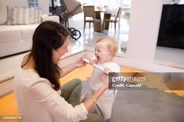 mother helping down syndrome baby to stand up - down syndrome baby stock pictures, royalty-free photos & images