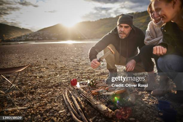 family having barbecue at a riverbank - couple grilling stock-fotos und bilder