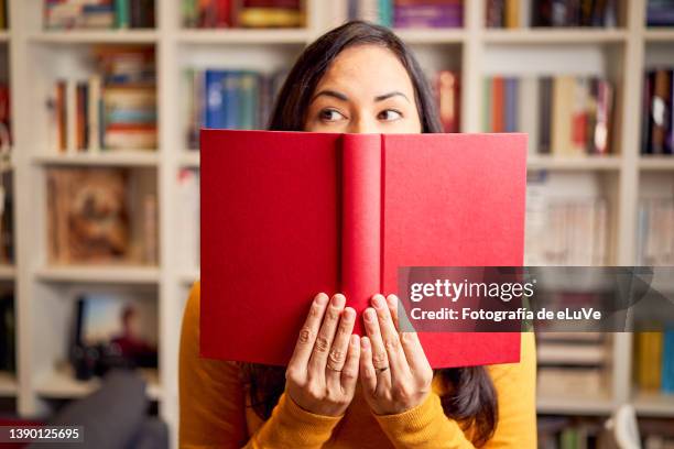 female young behind book with face covered for a red book - at a glance ストックフォトと画像