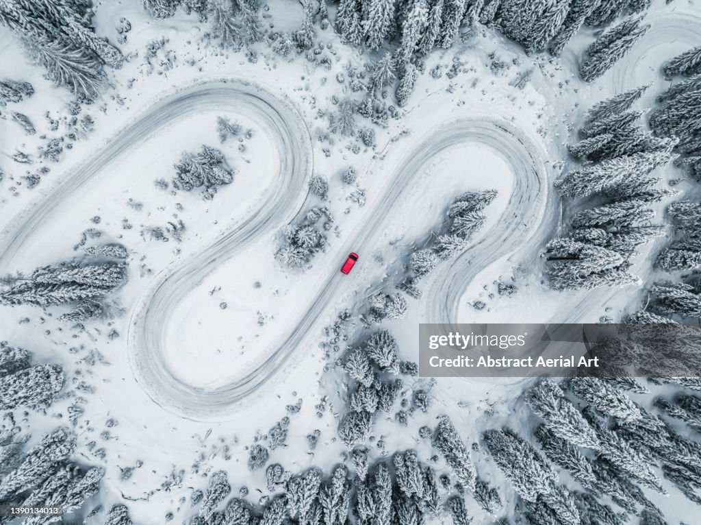 Camper van driving on a winding road through a snow covered forest seen from directly above, Dolomites, Italy