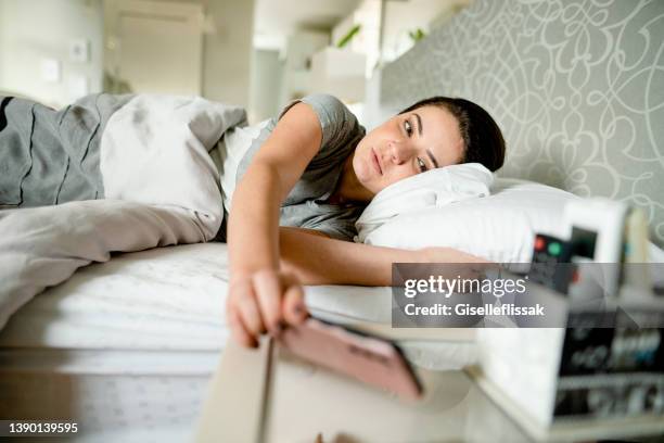 woman waking up in bed and turning off her alarm - sleep routine stock pictures, royalty-free photos & images