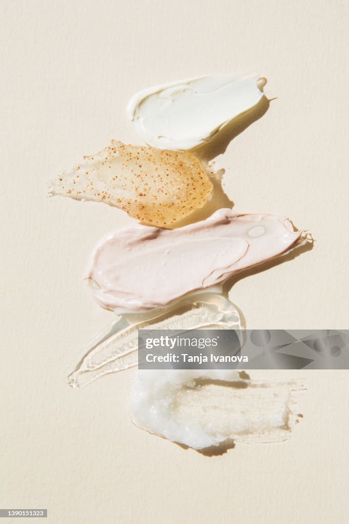 Textured multi colored smears of cosmetics on a beige background. Samples of creams, face mask, scrub with exfoliating particles, face gel, serum. Flat lay, top view.