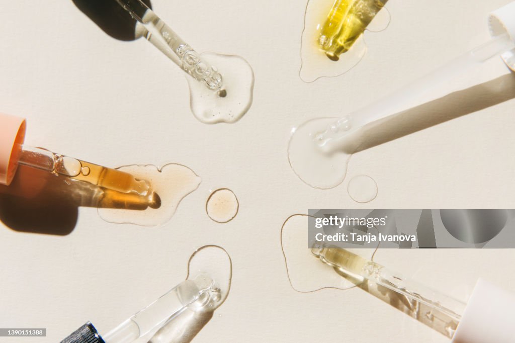 Pipettes with drops of cosmetic liquid on beige background. Beauty product with peptides, ceramides, hyaluronic gel, polyglutamic acid, essential oil, CBD, retinol, collagen. Multitasking beauty. Flat lay, top view.