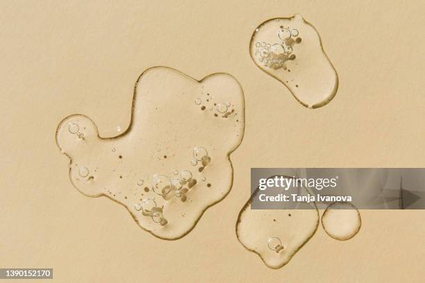 transparent drops of serum on beige background. liquid hyaluronic acid gel. flat lay, top view. - jojoba stockfoto's en -beelden