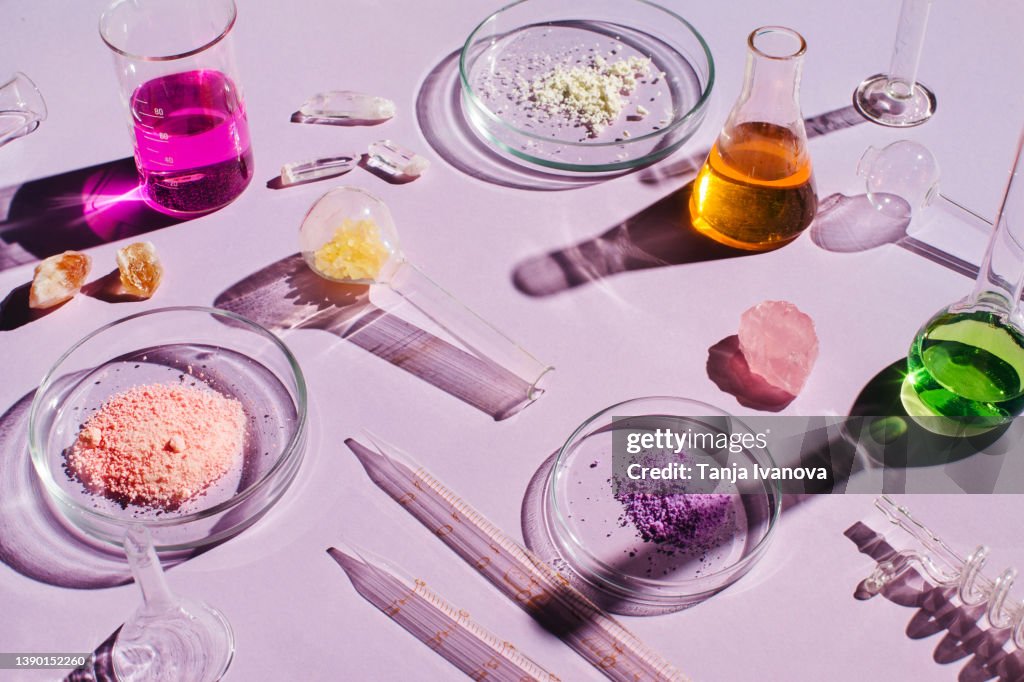 Colorful background with laboratory utensils, samples of cosmetics and glass vials on a purple background. Natural medicine, cosmetic research, bio science, organic skin care products. Top view, flat lay.