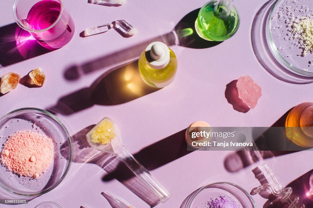 Colorful background with laboratory utensils, samples of cosmetics and glass vials on a purple background. Natural medicine, cosmetic research, bio science, organic skin care products. Top view, flat lay.