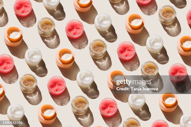 pattern of glass jars with facial moisturizer, face mask, scrub with exfoliating particles on a beige background. concept of body care and beauty. top view, flat lay - cremas faciales fotografías e imágenes de stock