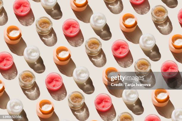 pattern of glass jars with facial moisturizer, face mask, scrub with exfoliating particles on a beige background. concept of body care and beauty. top view, flat lay - scrubs stock pictures, royalty-free photos & images