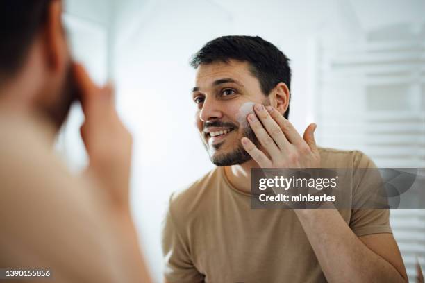 handsome man applying face cream in the bathroom - skin care stock pictures, royalty-free photos & images