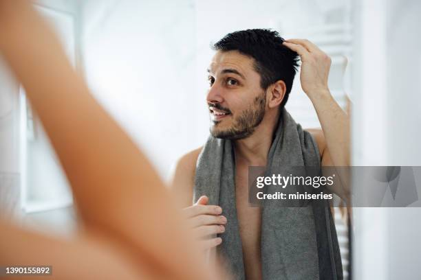 handsome man styling his hair in a bathroom - hand in hair stock pictures, royalty-free photos & images