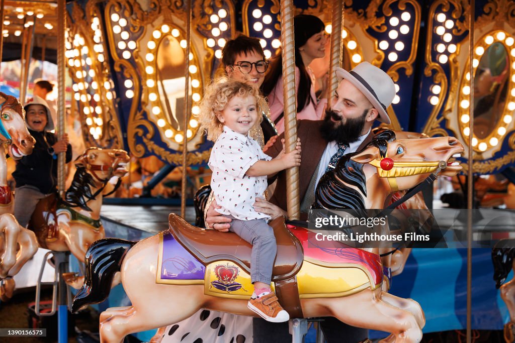 Parents ride carousel with toddler son