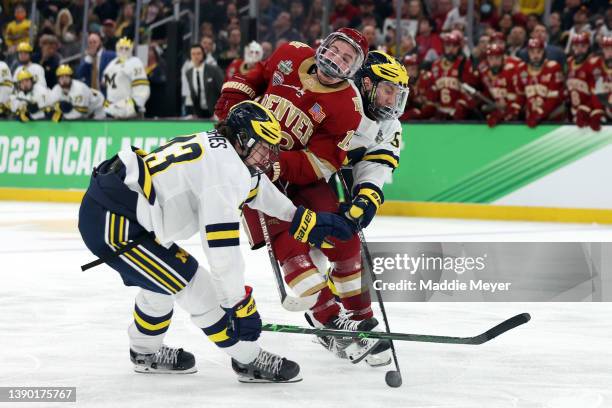 Massimo Rizzo of the Denver Pioneers collides with Luke Hughes of the Michigan Wolverines and Garrett Van Wyhe during overtime of the Frozen Four...
