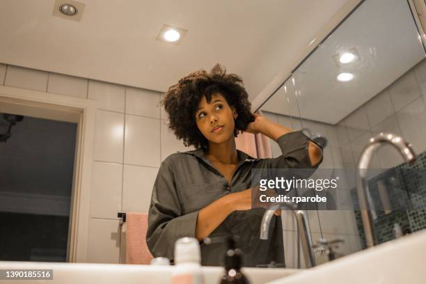 nel bagno, una giovane donna nera si aggiusta i capelli - frizzy hair foto e immagini stock