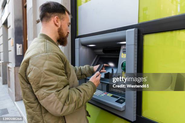 young man with smart phone using atm - atm 個照片及圖片檔