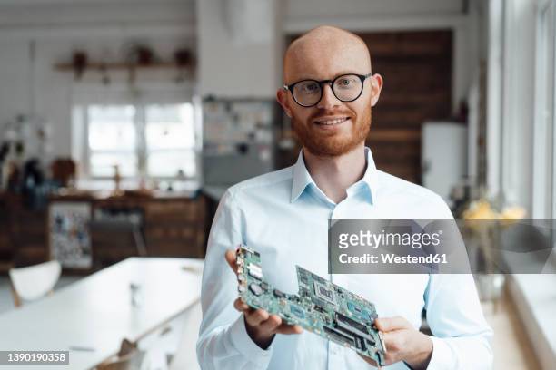 smiling young businessman standing with circuit board in office - computerteil stock-fotos und bilder
