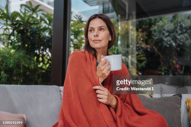 contemplative woman with coffee cup wrapped in blanket in yard - wrapped in a blanket stock pictures, royalty-free photos & images
