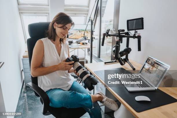 smiling photographer checking camera sitting on chair in studio - photographer imagens e fotografias de stock