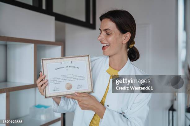 happy female doctor holding certificate in clinic - accreditation stock-fotos und bilder