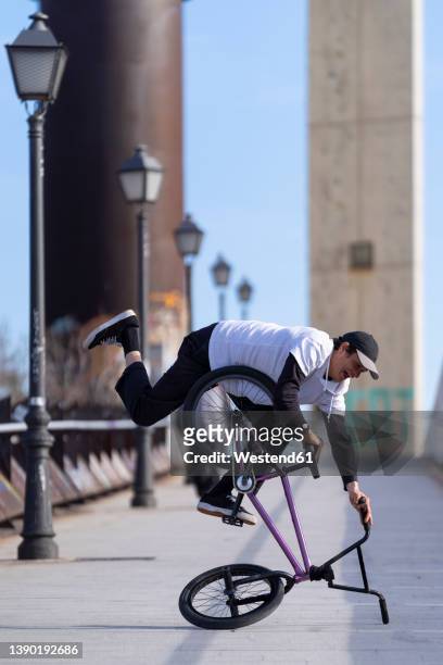 man doing stunt with bicycle on street in city - wheelie stock-fotos und bilder