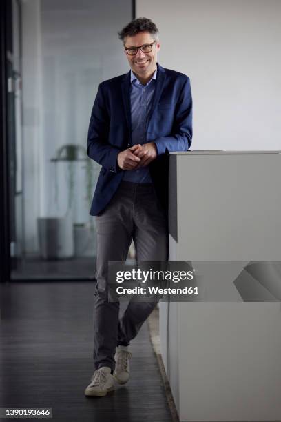 happy businessman wearing eyeglasses leaning on desk in office - lean imagens e fotografias de stock