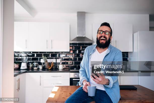freelancer with smartphone and coffee cup laughing at home - man with iphone stock pictures, royalty-free photos & images