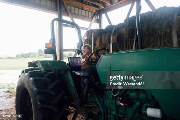 happy boy sitting on tractor's driving seat in farm - driver's seat stock pictures, royalty-free photos & images